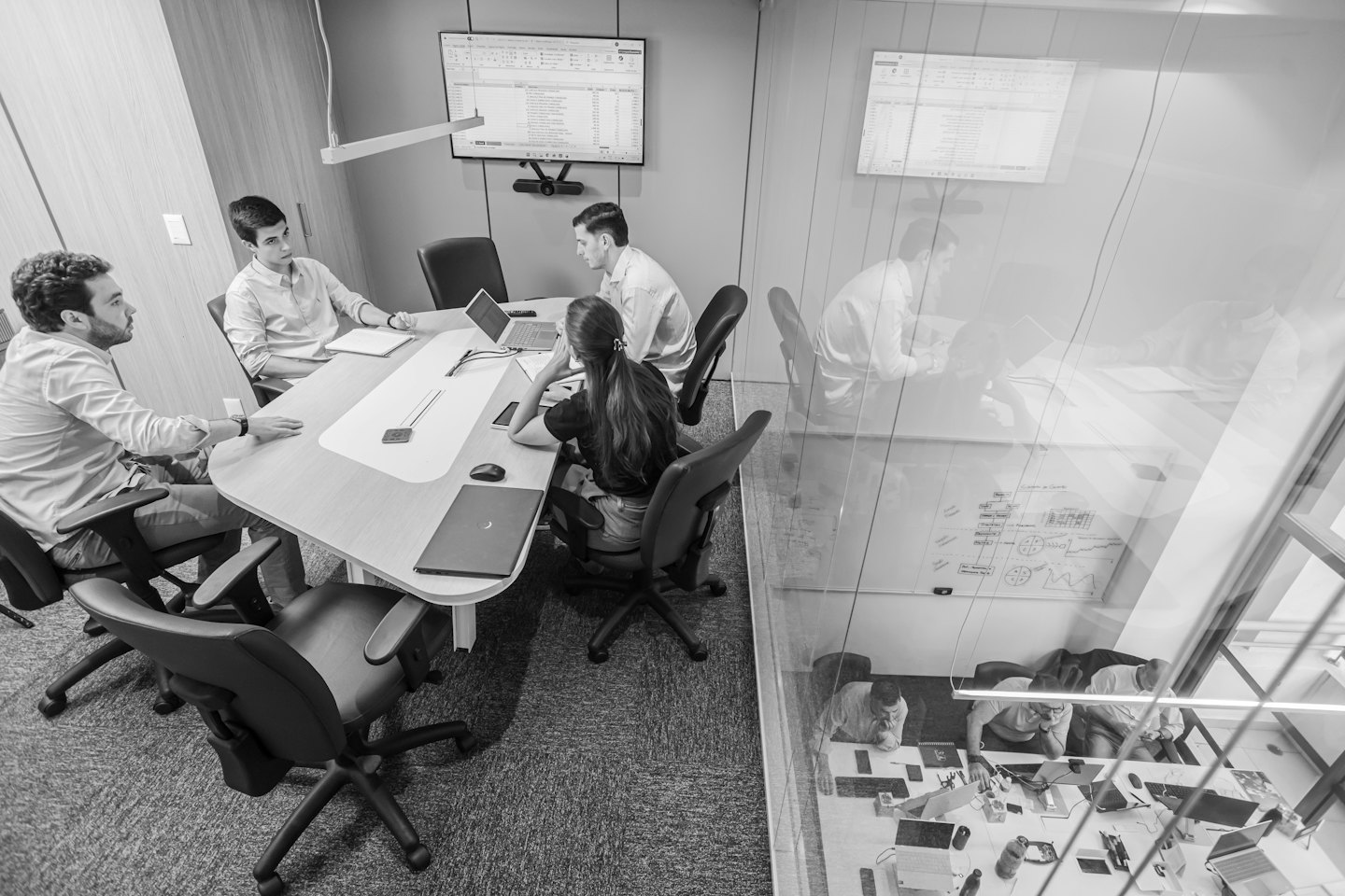 Professionals werken samen rond een vergadertafel met laptops en een spreadsheet.