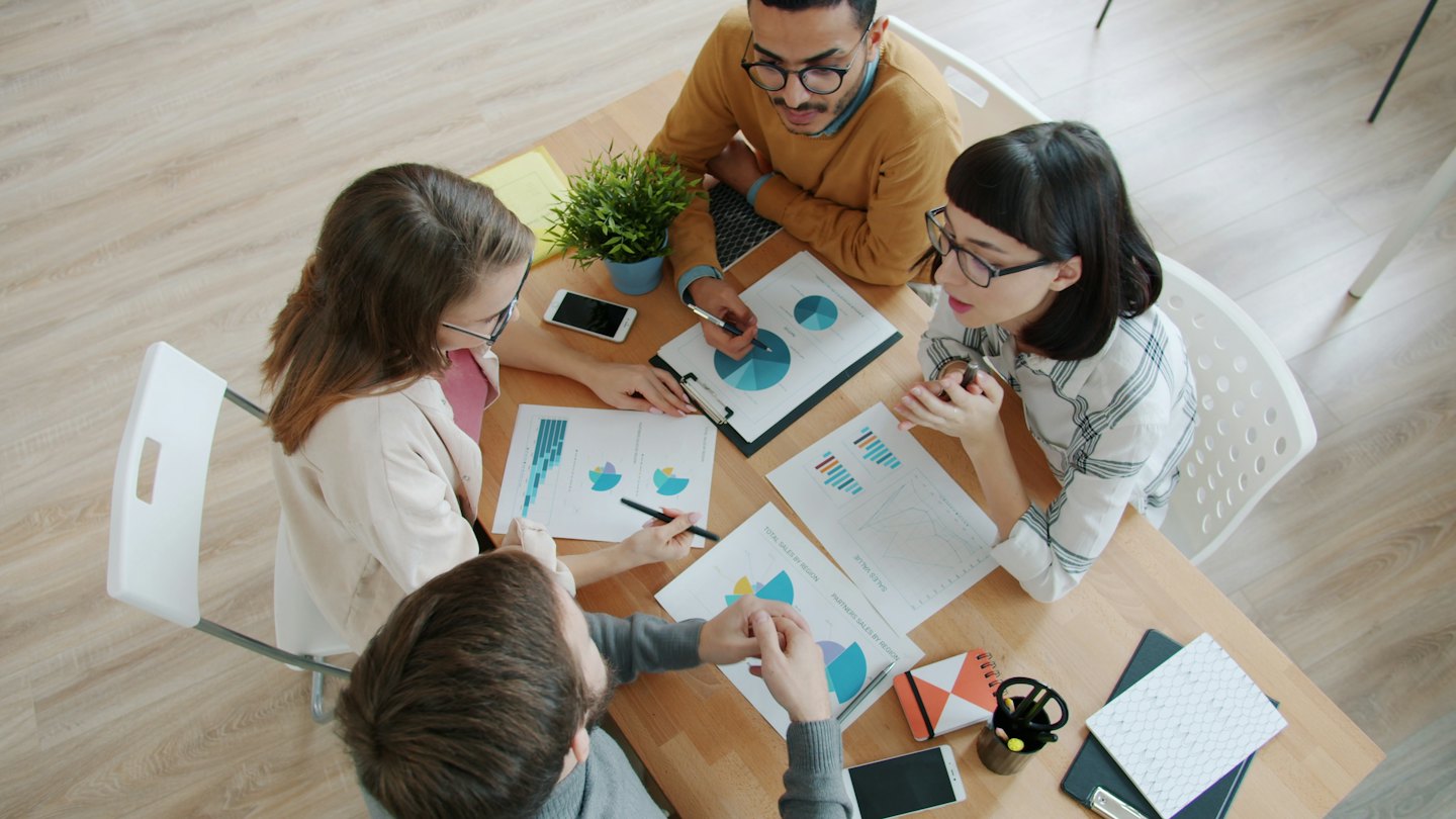 Diverse professionals bespreken grafieken en diagrammen aan een vergadertafel.